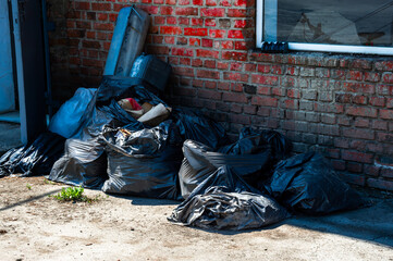 Several black trash bags stuffed with waste are stacked against a red brick wall in a commercial setting, highlighting urban litter issues