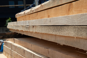 Sunlight illuminates neatly stacked wooden planks at a construction site, showcasing the texture and grain of the wood in clear detail