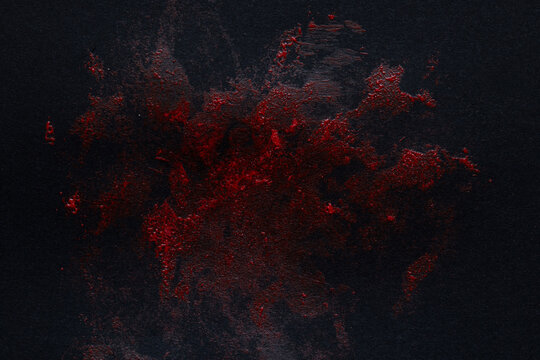 Red textured paint stain on black background as a smear resembling blood for design, horror, background, texture