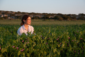 Young woman smiling and enjoying sunset in a field of green peas