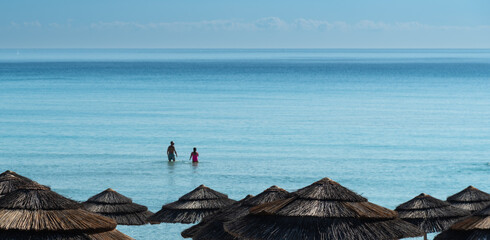 Tourists walking in crystal clear water with beach umbrellas in the foreground