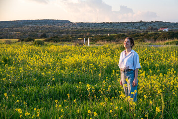 Young woman standing smiling and enjoying sunset in blooming yellow field