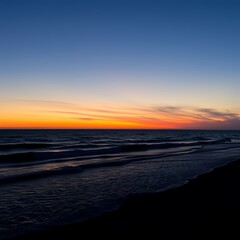 Fototapeta premium Vibrant orange and blue sunset over dark ocean waves