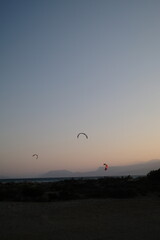 Several kitesurfers ride along the Turkish coastline at sunset. The silhouettes of kites contrast beautifully against the pastel evening sky. Ideal for themes of sport, freedom, beach holidays, and ac