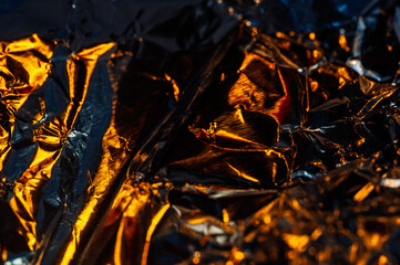 Close-up of crumpled aluminum foil, reflecting warm, golden light. The contrasting shadows and...