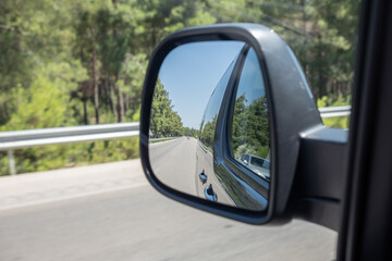 Reflection of a Road and Trees in a Side Mirror While Driving Along a Scenic Route in Bright...