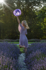 A woman in a lilac dress dances joyfully through a lavender field, her arm raised high holding a...