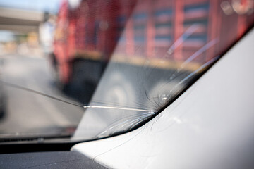 Cracked Windshield Near Busy Roadway With Large Truck in Background During Daylight Hours