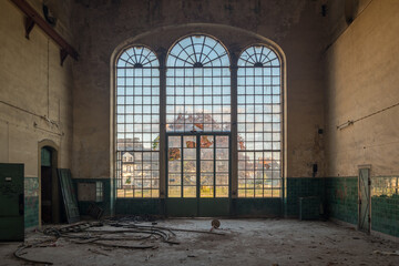 Interior of an abandoned industrial building with large arched windows and scattered debris,...