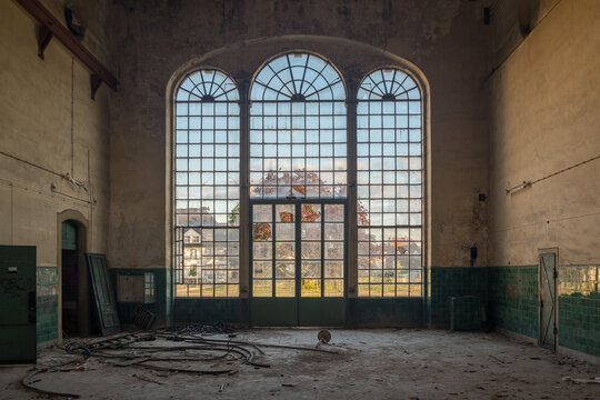Interior of an abandoned industrial building with large arched windows and scattered debris, showcasing urban decay and forgotten architecture