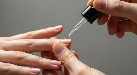 Close-up of hands applying nail oil with a dropper to fingernails for cuticle care and moisturizing against a neutral background.