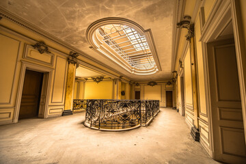 Ornate abandoned villa interior with intricate wrought iron railing and large skylight, showcasing...
