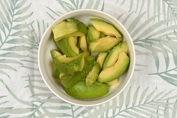 A bowl of sliced avocado on a palm leaf patterned tablecloth