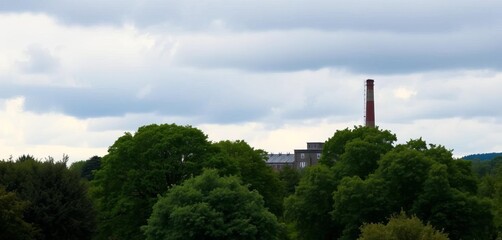 Obraz premium Overcast sky above lush green landscape, trees leading to old industrial building with tall chimney near Green Lane, Manningham, Bradford, urban, derelict