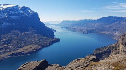 Panoramic view of a serene lake nestled within a majestic mountain valley, partially snow-capped peaks rising in the distance under a clear blue sky