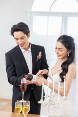 Asian Wedding couple pouring champagne into glasses, celebration, happiness, bride and groom smiling, elegant dress and suit, romantic moment