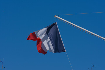 A vibrant French flag with vertical red, white, and blue stripes proudly waves against a clear,...
