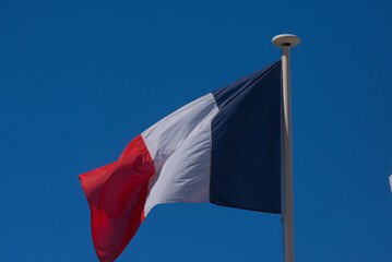 A vibrant French flag with vertical red, white, and blue stripes proudly waves against a clear,...