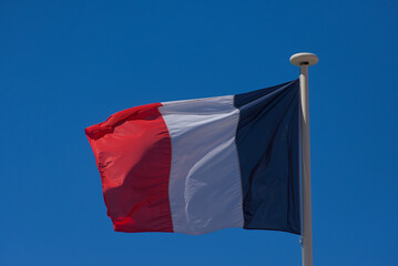 A vibrant French flag with vertical red, white, and blue stripes proudly waves against a clear,...
