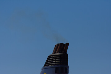 Dark smoke billows from multiple large exhaust funnels of a ship, starkly contrasted against a...