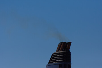 Dark smoke billows from multiple large exhaust funnels of a ship, starkly contrasted against a...