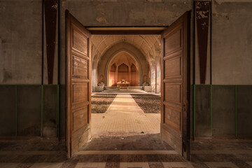 View through open wooden doors into an abandoned, decayed chapel interior with arched ceiling and...