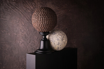 Sfere decorative su piedistallo con texture metallica e pietra su fondo materico marrone