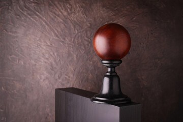Sfera decorativa in legno su piedistallo nero con sfondo materico marrone