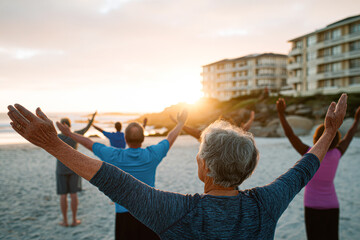 A group of people practicing yoga or stretching with arms raised on a beach during sunrise near beachfront buildings.