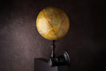 Grande sfera in marmo giallo con venature su piedistallo nero e sfondo marrone materico