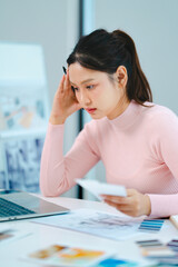 Stressed office woman reading document with worried face and messy paperwork on desk in workplace