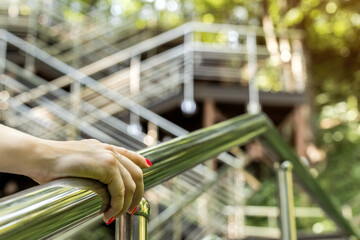 woman climbing stairs in park holding onto handrail. a woman's hand holds onto a handrail. stairs in the park. stairs leading up the hill