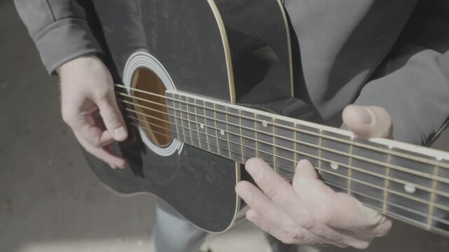 Man in black jacket playing six-string guitar, close-up