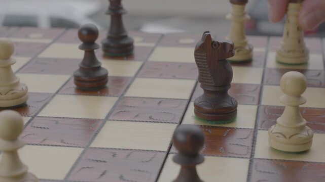 The hand of a person moving a knight chess piece on a board.