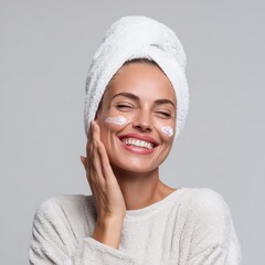 A young woman enjoys self-care, applying cream to her face. She exudes a sense of peace and rejuvenation while wearing a towel and smiling.