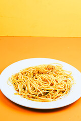 A classic plate of spaghetti with a rich, savory meat sauce, served on a white dish against an orange background.