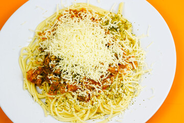 A generous serving of spaghetti bolognese topped with a mound of shredded cheese and herbs.