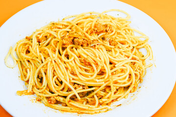 A classic plate of spaghetti with a rich, savory meat sauce, served on a white dish against an orange background.