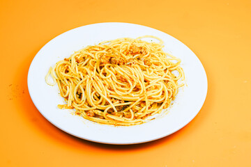 A classic plate of spaghetti with a rich, savory meat sauce, served on a white dish against an orange background.