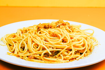 A classic plate of spaghetti with a rich, savory meat sauce, served on a white dish against an orange background.