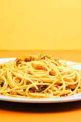 A classic plate of spaghetti with a rich, savory meat sauce, served on a white dish against an orange background.