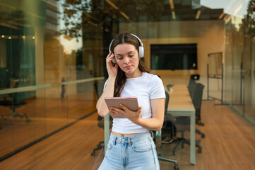 Young woman wearing headphones using digital tablet outside modern office building