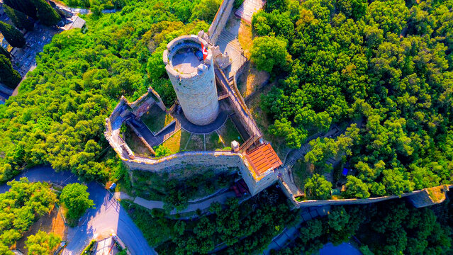 Aerial view of the Ancient Castle of Monte Ursino, on top of a hill, ancient elements and buildings of the original settlement of Noli. fpv. Red flag with a cross on the towers. Noli Italy 02.08.2025