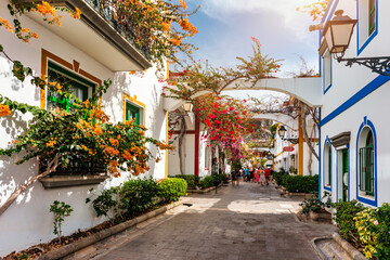 Fototapeta premium Street with blooming flowers in Puerto de Mogan, Gran Canaria, Spain. Favorite vacation place for tourists and locals on island. Puerto de Mogan with lots of bougainvillea flowers, Canary Island.