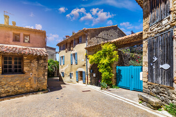 Charming narrow street in Venasque with sunlit stone and vibrant flowers, Provence, France. Narrow street in picturesque village of Venasque features stone buildings adorned with vibrant flowers.