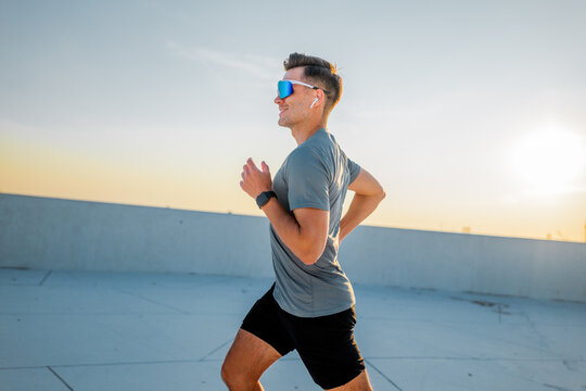 Joyful runner embraces sunset vibes on rooftop during evening exercise session