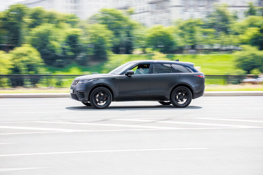 View from the side of Range Rover Velar automobile moving fast in city. Blured road with trees in distance on high speed.