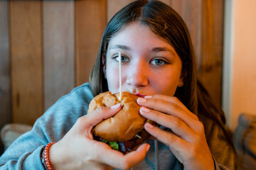 Pretty teenager devouring a hamburger and fries in a fast food restaurant