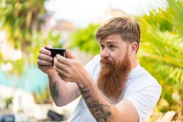 Redhead man with beard playing with the mobile phone