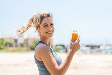 Young pretty sport woman holding an orange juice at outdoors smiling a lot